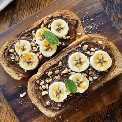 To make Chocolate Hazelnut Banana Toast, gather these simple ingredients: - 2 slices of whole-grain bread - 2 tablespoons chocolate hazelnut spread - 1 ripe banana, sliced - 1 tablespoon chopped hazelnuts - 1 tablespoon chia seeds - 1 teaspoon honey or maple syrup (optional) - A pinch of sea salt - Fresh mint leaves for garnish (optional) With these ingredients, you set the stage for a tasty breakfast. Whole-grain bread gives you fiber. The chocolate hazelnut spread adds a rich, sweet flavor. A ripe banana brings natural sweetness and creaminess. Chopped hazelnuts and chia seeds add a nice crunch. Honey or maple syrup can boost the sweetness if you want. A pinch of sea salt enhances all the flavors. And fresh mint leaves can brighten up your toast. This recipe is quick and easy, perfect for busy mornings. If you want more details, check the Full Recipe. Enjoy your cooking! Start by toasting your whole-grain bread. Place the slices in the toaster. Set it to medium heat. Wait until the bread turns golden brown and crispy. This gives the toast a nice crunch. If you like it darker, toast a bit longer. Keep an eye on it, so it does not burn. The perfect toast sets the stage for the rest of the dish. Next, grab your ripe banana. Place it on a cutting board. Use a sharp knife to slice it into even rounds. Aim for slices about a quarter-inch thick. If the slices are too thin, they may break when you layer them. If they're too thick, they won't fit well on the toast. Even slices help each bite taste great. Now it’s time to put everything together. Take your golden toast and spread one tablespoon of chocolate hazelnut spread on each slice. Make sure to cover the toast evenly. Then, layer the banana slices on top. Distribute the banana evenly across the spread. This helps balance the flavors. Sprinkle the chopped hazelnuts and chia seeds over the bananas. They add nice crunch and nutrition. If you like it sweeter, drizzle a teaspoon of honey or maple syrup on top. This step is optional, but it makes the toast even tastier. Finish with a pinch of sea salt to enhance the flavors. If you want, garnish with fresh mint leaves. They add a pop of color and a refreshing aroma. For the full recipe, check out the details above. Enjoy your delightful breakfast bite! To make your chocolate hazelnut banana toast look great, serve it on a wooden board or a bright plate. Cut the toast in half diagonally. Arrange the halves in a fan shape. Add a few extra banana slices and hazelnuts around the toast. This will create a lovely display for photos and impress your friends. Feel free to swap out the whole-grain bread for another type you like. You can also change the chocolate hazelnut spread to a nut-free option if needed. If you prefer less sweetness, skip the honey or syrup. You can add more toppings, too. Try coconut flakes or berries for new flavors. Using whole-grain bread offers more fiber and nutrients than white bread. Hazelnuts provide healthy fats, protein, and vitamins. Bananas are packed with potassium and fiber. Chia seeds add omega-3 fatty acids and antioxidants. These ingredients make this toast not just tasty but also a smart choice for breakfast. For the full recipe, check the earlier section. {{image_2}} If you want a nut-free option, try using sunflower seed butter or soy nut butter. Both spreads taste great and keep the texture creamy. You can also use coconut cream for a rich, smooth flavor. Each will give you a delicious twist while keeping it safe for those with nut allergies. For a protein boost, spread some almond or peanut butter under the chocolate hazelnut spread. You can also mix protein powder into the spread. Just a scoop will give your toast a healthy kick without changing the taste much. This small change can help keep you full longer. Change up your toast with seasonal fruits. In summer, add fresh strawberries or blueberries for a burst of flavor. In fall, try slices of apple or pear with a sprinkle of cinnamon. Each season brings new fruits that can brighten your toast and keep it exciting. You can find more ideas in the Full Recipe. To keep your chocolate hazelnut banana toast fresh, store it properly. If you have leftovers, wrap them in plastic wrap or place them in an airtight container. Keep them in the fridge for up to two days. This helps maintain the bread's crispness and the banana's taste. If you notice the bread getting soggy, toast it again before eating. Mornings can be hectic. You can prep your chocolate hazelnut banana toast quickly. Spread the chocolate hazelnut spread on your bread the night before. Slice the banana and store it in a small container with a bit of lemon juice to prevent browning. In the morning, assemble your toast quickly. This saves you time while still giving you a tasty breakfast. You can freeze some components for later use. Toasted bread can be frozen for up to three months. Place slices in a freezer bag and separate them with parchment paper. For the banana, slice it and freeze the pieces on a baking sheet. Once frozen, put them in a bag. When you’re ready, just toast the bread and add the frozen banana slices directly on top. They will thaw quickly and taste great! Yes, you can use regular bread. However, whole-grain bread offers more fiber and nutrients. Fiber helps with digestion, making you feel full longer. Regular white bread may taste softer, but it lacks many health benefits. If you want a healthier choice, stick with whole-grain bread. It adds texture and flavor to your chocolate hazelnut banana toast. To make this recipe vegan, swap honey for maple syrup. Maple syrup is a great choice and tastes sweet. Ensure your chocolate hazelnut spread is dairy-free. Many brands now offer vegan options. Check the label to confirm. You can still enjoy this tasty toast without using animal products. For the best chocolate hazelnut spread, I recommend brands like Nutella or Justin's. Nutella is creamy and sweet, while Justin's has a more nutty flavor. If you want to try making your own, blend roasted hazelnuts, cocoa powder, and a sweetener of your choice. This way, you can control the taste and ingredients. In this blog post, we covered a delicious chocolate hazelnut toast recipe. We detailed the ingredients, from whole-grain bread to toppings like banana and hazelnuts. You learned step-by-step instructions for toasting the bread and assembling your dish. We discussed tips for presentation, customization, and health benefits. Finally, we shared storage methods and common FAQs. Creating this recipe is simple and fun. You can impress anyone with your tasty toast! Enjoy making it your own. Happy cooking!